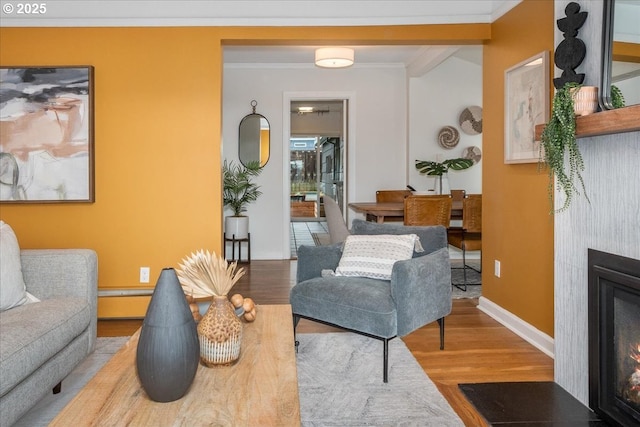 living room featuring wood finished floors, baseboards, a glass covered fireplace, crown molding, and baseboard heating