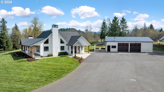 view of front of home featuring a garage, a front lawn, a chimney, and an outbuilding