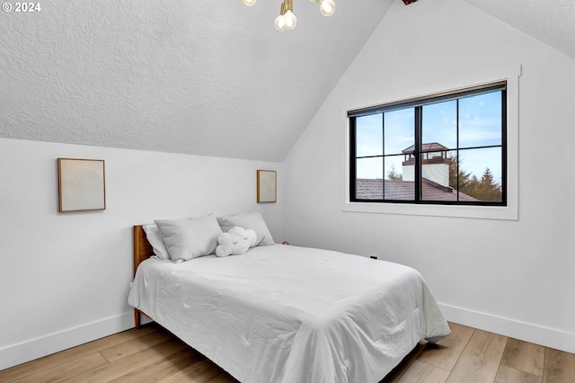 bedroom with a textured ceiling, baseboards, vaulted ceiling, and wood finished floors