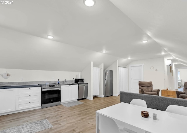 kitchen featuring lofted ceiling, appliances with stainless steel finishes, dark countertops, and light wood-style floors