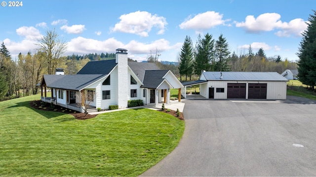 modern farmhouse style home with a chimney, a detached garage, a porch, an outbuilding, and a front lawn