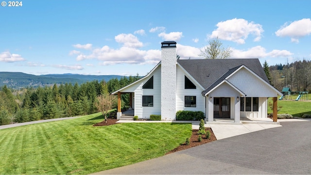 view of front of property featuring a shingled roof, a chimney, a front lawn, and a wooded view