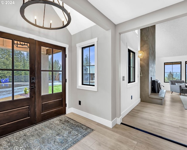 entryway featuring baseboards, vaulted ceiling, french doors, light wood-style floors, and a chandelier