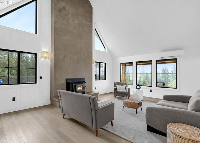 living area featuring high vaulted ceiling, baseboards, a wall unit AC, and light wood finished floors