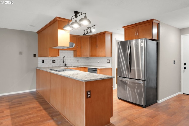 kitchen featuring pendant lighting, tasteful backsplash, light hardwood / wood-style floors, kitchen peninsula, and stainless steel refrigerator