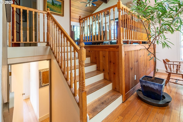 staircase with lofted ceiling, hardwood / wood-style floors, a ceiling fan, and baseboards