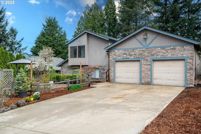 tri-level home featuring fence, a garage, concrete driveway, and stone siding