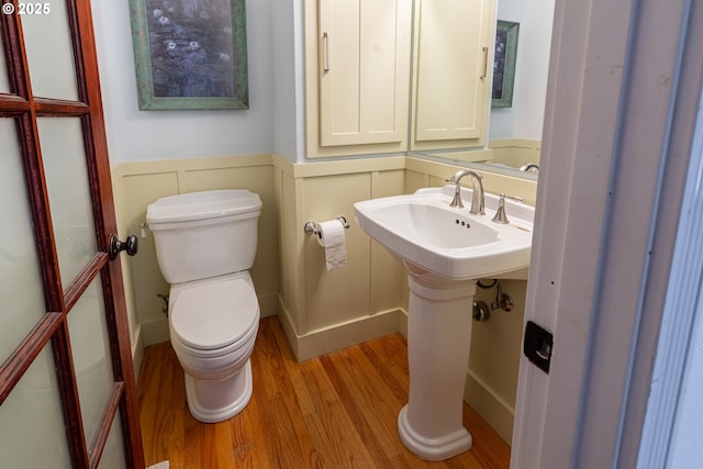 bathroom with a sink, a decorative wall, a wainscoted wall, toilet, and wood finished floors