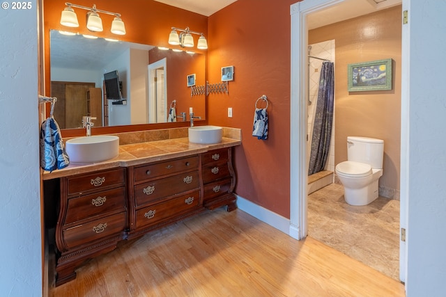 bathroom featuring baseboards, toilet, double vanity, and a sink