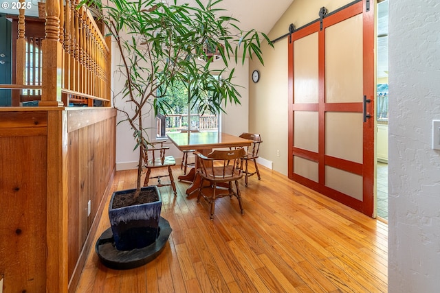 dining space featuring baseboards, a barn door, light wood-style floors, and vaulted ceiling