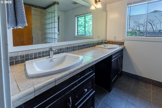 full bathroom with visible vents, a tile shower, double vanity, and a sink