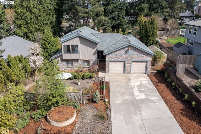 view of front of home featuring a garage, driveway, stone siding, roof with shingles, and fence