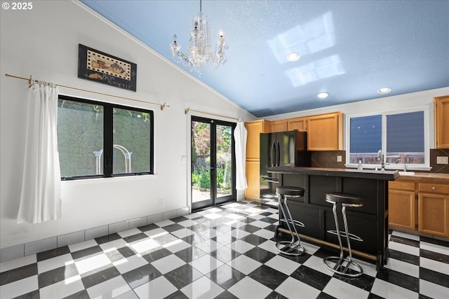 kitchen with vaulted ceiling, freestanding refrigerator, dark countertops, backsplash, and a chandelier