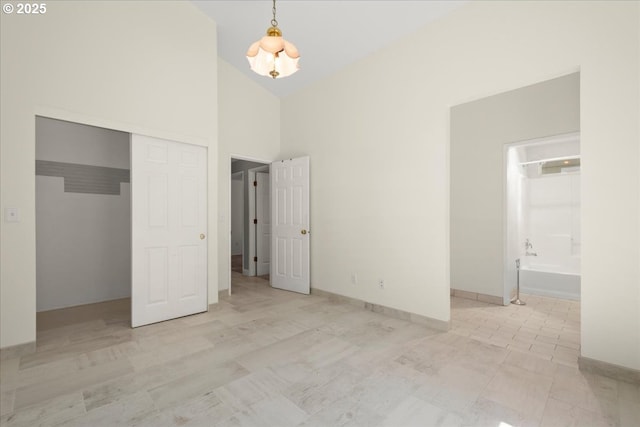 unfurnished bedroom with high vaulted ceiling, a closet, ensuite bath, baseboards, and a chandelier