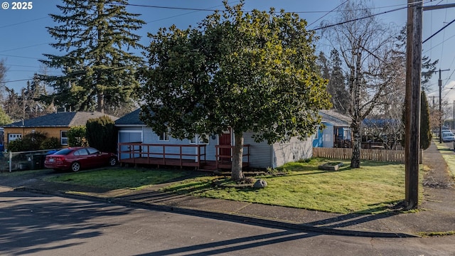 view of property hidden behind natural elements with a deck, a front yard, and fence