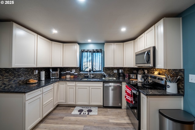 kitchen featuring dark stone counters, appliances with stainless steel finishes, light wood-type flooring, and a sink