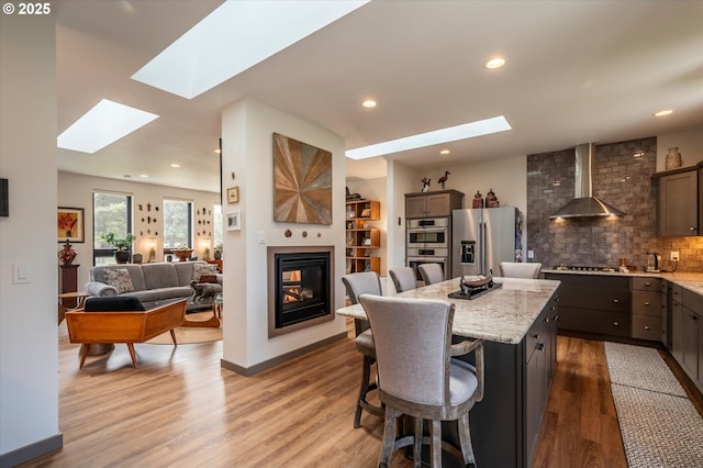 1342 11th St SW, Bandon, OR 97411 - kitchen with appliances with stainless steel finishes, wall chimney exhaust hood, a skylight, a breakfast bar, and wood finished floors