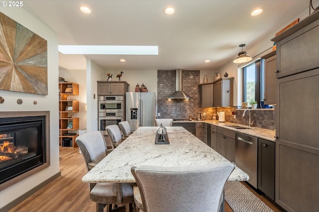 1342 11th St SW, Bandon, OR 97411 - kitchen featuring stainless steel appliances, wall chimney range hood, decorative backsplash, wood finished floors, and a breakfast bar