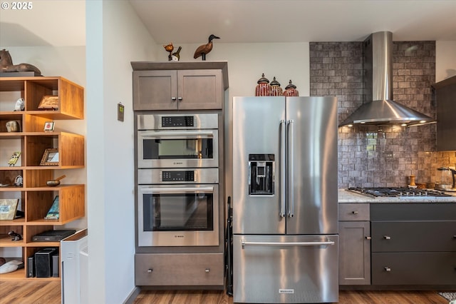 1342 11th St SW, Bandon, OR 97411 - kitchen featuring stainless steel appliances, wall chimney range hood, wood finished floors, decorative backsplash, and light stone countertops