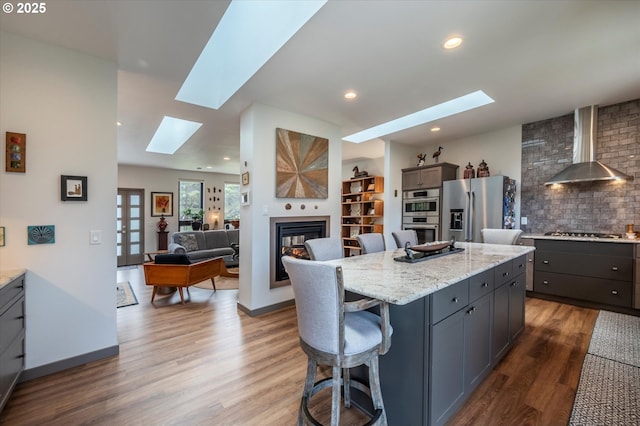 1342 11th St SW, Bandon, OR 97411 - kitchen featuring a skylight, wall chimney exhaust hood, stainless steel appliances, a breakfast bar, and wood finished floors