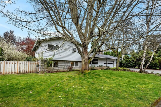 back of property with an attached garage, fence, and a yard