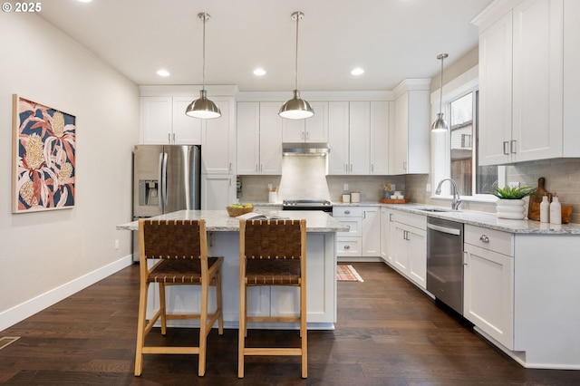 kitchen featuring a kitchen island, appliances with stainless steel finishes, white cabinetry, hanging light fixtures, and light stone countertops