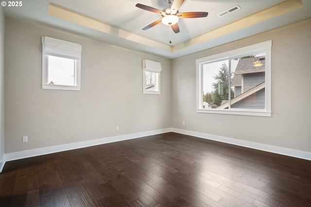 empty room featuring dark hardwood / wood-style flooring, a tray ceiling, and ceiling fan