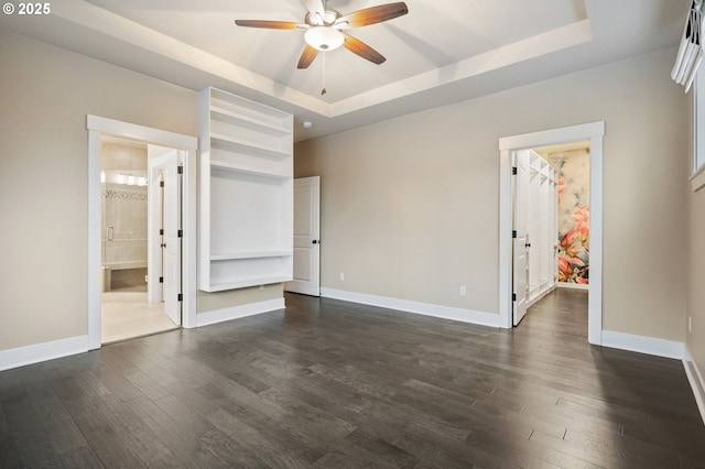 unfurnished bedroom with ensuite bathroom, dark hardwood / wood-style floors, a spacious closet, ceiling fan, and a raised ceiling