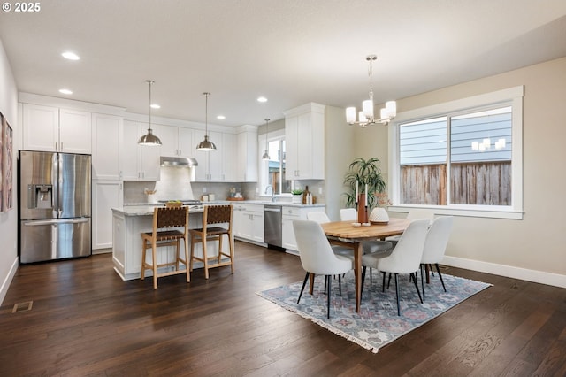 dining space with sink, a healthy amount of sunlight, dark wood-type flooring, and a notable chandelier