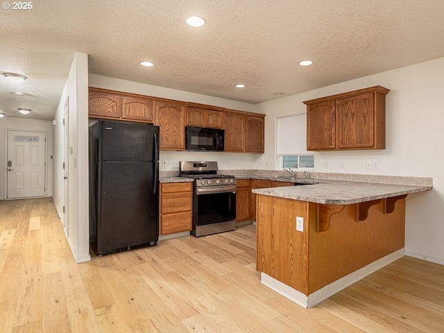 kitchen with a breakfast bar area, a textured ceiling, kitchen peninsula, light hardwood / wood-style floors, and black appliances