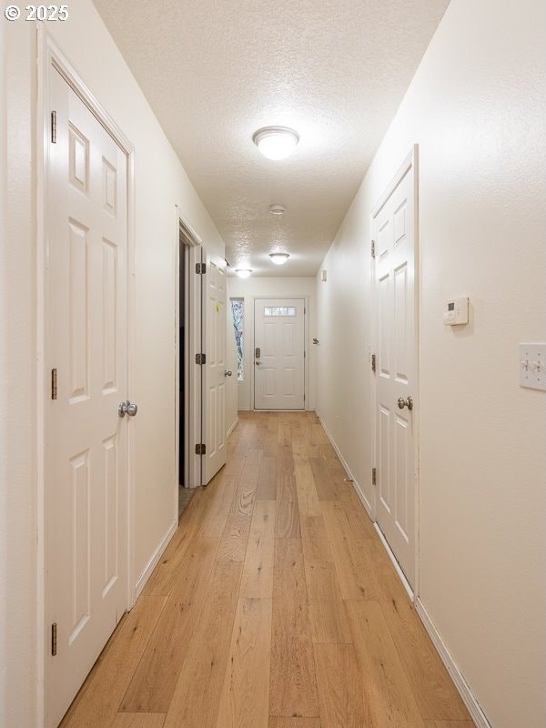 hall with a textured ceiling and light hardwood / wood-style flooring