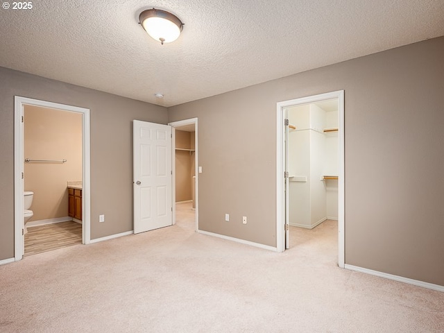 unfurnished bedroom featuring ensuite bath, a spacious closet, light carpet, a textured ceiling, and a closet