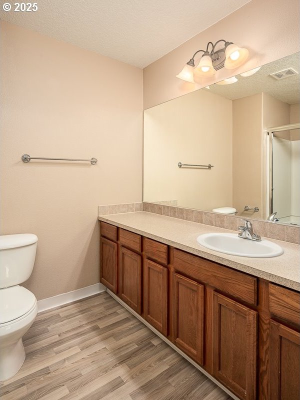 bathroom featuring hardwood / wood-style flooring, vanity, an enclosed shower, toilet, and a textured ceiling