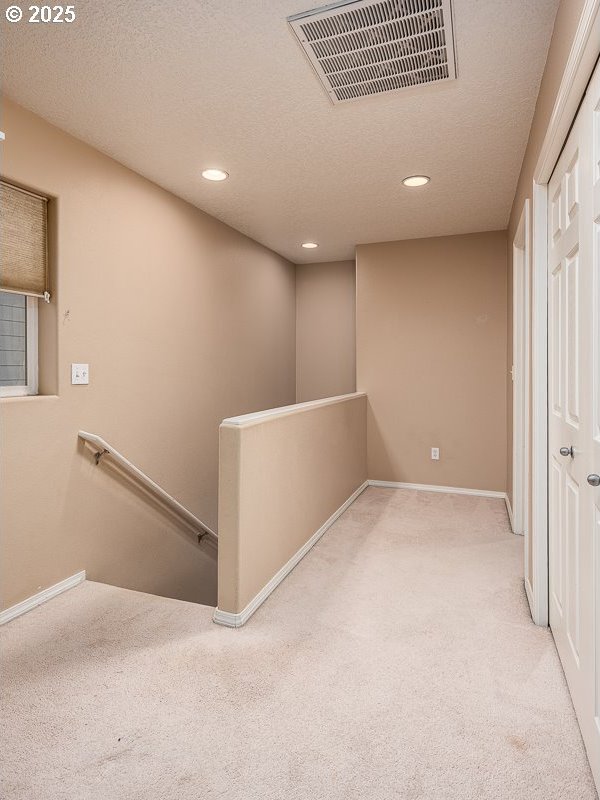 corridor with light colored carpet and a textured ceiling