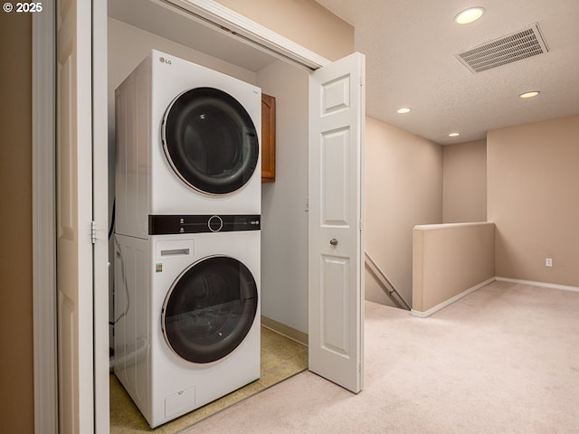 laundry area featuring light colored carpet, a textured ceiling, and stacked washer / dryer