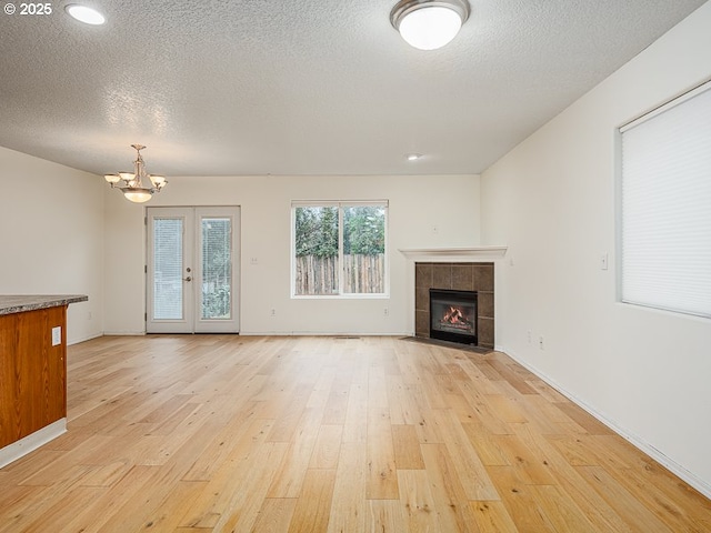 unfurnished living room with a fireplace, french doors, a textured ceiling, and light wood-type flooring