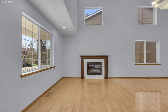 13007 SE Raymond Ct, Portland, OR 97236 - unfurnished living room featuring plenty of natural light, wood finished floors, a glass covered fireplace, baseboards, and a towering ceiling
