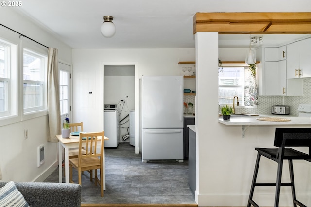 kitchen featuring light countertops, backsplash, freestanding refrigerator, a sink, and plenty of natural light