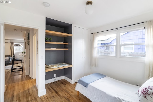 bedroom featuring built in study area, baseboards, and wood finished floors