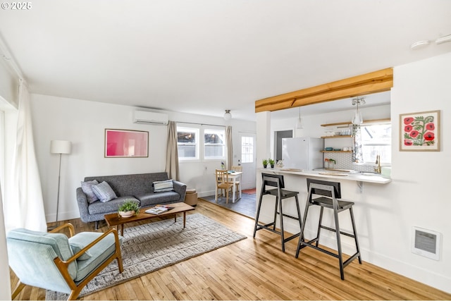 living area featuring light wood-style floors, a wall mounted air conditioner, visible vents, and baseboards