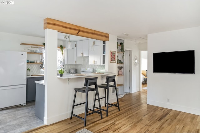 kitchen featuring tasteful backsplash, a breakfast bar area, freestanding refrigerator, light countertops, and open shelves