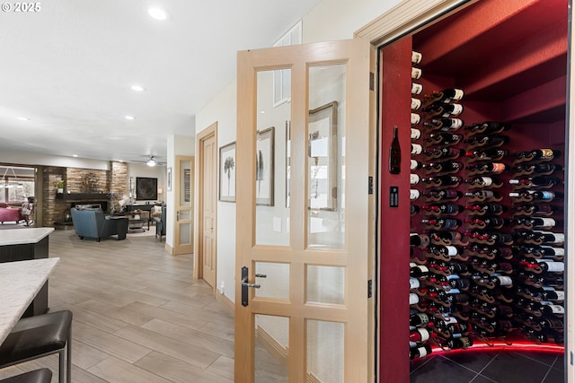 wine room featuring wood-type flooring, a stone fireplace, and ceiling fan