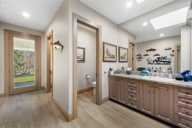 bathroom featuring wood-type flooring, toilet, a skylight, and vanity