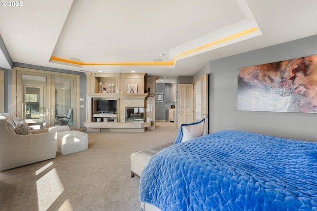 carpeted bedroom featuring a raised ceiling, a fireplace, and french doors