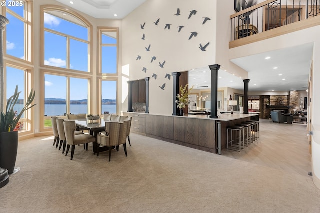 carpeted dining room featuring ornate columns, a water view, and a high ceiling