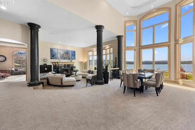 carpeted living room featuring ornate columns, a water view, a wood stove, a fireplace, and a high ceiling