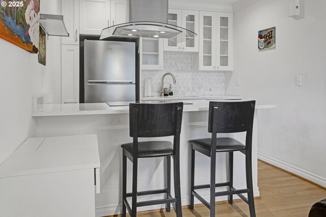 7522 SW Barnes Rd Unit H, Portland, OR 97225 - kitchen featuring freestanding refrigerator, wall chimney exhaust hood, tasteful backsplash, white cabinetry, and light countertops