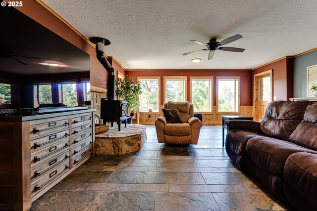 86561 R R Baker Rd, Springfield, OR 97478 - living room featuring a ceiling fan, a wood stove, stone tile flooring, crown molding, and wainscoting