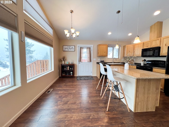 kitchen with a breakfast bar area, hanging light fixtures, a center island, black appliances, and light brown cabinets