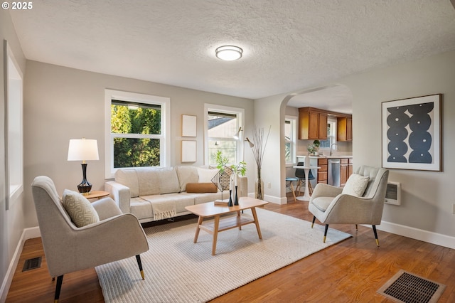 living room with heating unit, sink, a textured ceiling, and light hardwood / wood-style floors